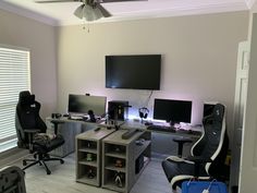 a home office with two computer monitors and a laptop on a desk in front of a flat screen tv