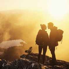 two people standing on top of a mountain looking at the sky and clouds in the distance