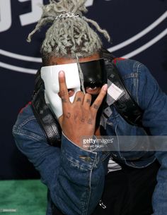 a man with dreadlocks on his head talking on a cell phone in front of a wall