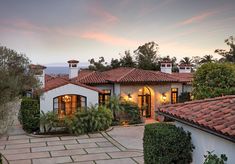 a house with red tile roofing surrounded by greenery and palm trees at dusk