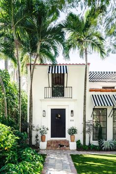 a white house with black and white striped awnings on the front door is surrounded by palm trees