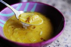 a spoonful of soup is in a purple bowl