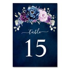 a table number card with flowers and leaves on the front, in navy blue background