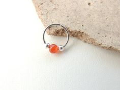 an orange beaded ring sitting on top of a rock next to a white wall