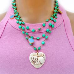 Handcrafted truly one-of-a-kind unique necklace, a vintage hand carved doggie on a heart shaped ox-bone pendant, little square shaped turquoise charms throughout, an evil eye a tiny moon sliver in pave crystals and a silk tassel all on a green vintage enamel chain measuring 38” long. Wear it long, doubled or tripled in any way creative way you like. Necklace is 38" in length Hand-carved heart pendant Variety of different charms Vintage enamel chain Made with love in Los Angeles Complimentary gif Whimsical Green Charms Jewelry, Whimsical Green Jewelry With Charms, Green Necklaces With Dangling Charms For Gifts, Green Necklaces With Dangling Charms As Gift, Green Necklace With Dangling Charms For Gift, Green Necklace With Dangling Charms As Gift, Green Bohemian Jewelry With Vintage Charm, Bohemian Green Necklaces With Charms, Bohemian Green Jewelry With Vintage Charm