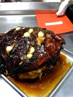 a large piece of meat sitting on top of a metal pan covered in sauce and nuts