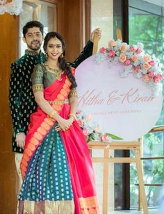 a man and woman standing next to each other in front of a sign with flowers on it