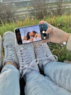 someone taking a selfie with their cell phone while sitting on the grass in front of some water