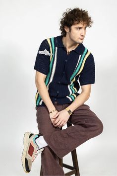 a man sitting on top of a stool wearing brown pants and a blue knitted shirt