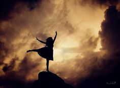 a woman standing on top of a rock with her arms in the air