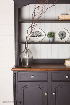 an old china cabinet with two vases and some books on the top shelf in front of it