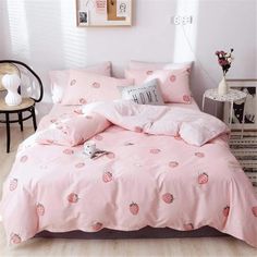 a bed with pink comforters and pillows in a room next to a chair, table and pictures on the wall