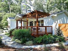 a small white house surrounded by trees and plants in front of a fenced off area