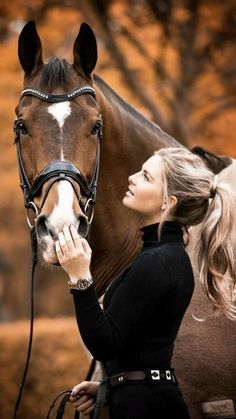 a woman standing next to a brown and white horse with her hand on the bridle