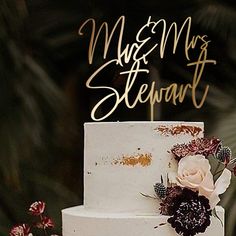 a white wedding cake with flowers on top and the words mr and mrs stewart above it