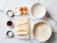 ingredients to make an egg cake laid out on a marble counter top with flour, eggs and butter