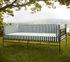 a black and white striped couch sitting on top of a lush green field next to a tree