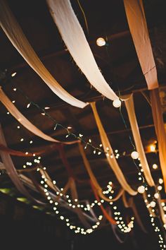 the lights are hanging from the ceiling above the tables at this wedding reception, which is decorated with white and gold streamers