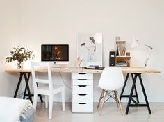 a desk with two chairs and a computer on top of it in a white room