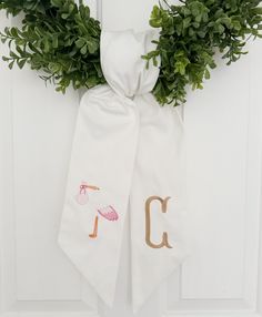 a white door hanger decorated with green leaves and an embroidered monogrammed initial