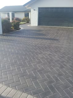 a brick driveway in front of a house with two garage doors on the other side