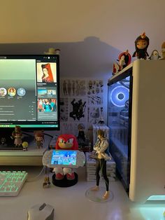 a desk with a computer monitor, keyboard and toy figurines