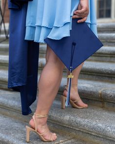 two people standing on steps with one holding a blue graduation cap and the other wearing heels