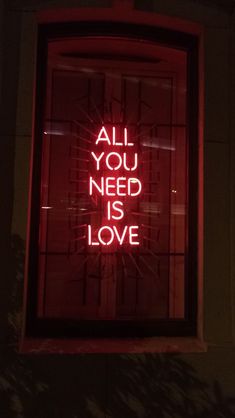 a red neon sign that says all you need is love on the side of a building