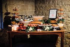 a wooden table topped with lots of pastries and desserts next to a stone wall