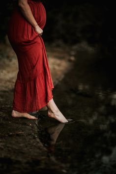 a pregnant woman in a red dress is standing in the water with her hands on her hips