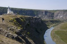 a man standing on top of a cliff next to a river and a church in the background