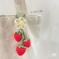 a crocheted strawberries hanging from a white tote bag with flowers on it