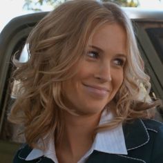 a woman with blonde hair smiling in front of a car