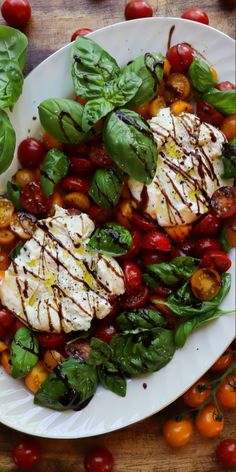 a white plate topped with chicken, tomatoes and spinach on top of a wooden table