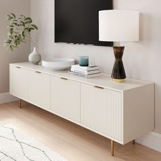 a television mounted on the wall above a white dresser with books and vases next to it