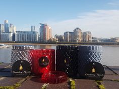 four different colored candles sitting on the ground next to some water and buildings in the background