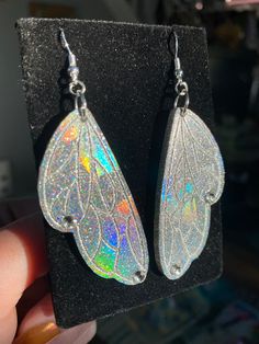 These gorgeous one of a kind  butterfly/fairy wing earrings are handmade with resin and are very lightweight. They are iridescent and holographic and will be sure to make a statement on your ears 💖 Handmade by Katie  KG Design & Decor Please follow my on social media  Instagram: @KG_DesignandDecor Facebook: KG Design and Decor Please be aware that this is handmade art and perfection has no place in art.  However, this was crafted with love and intention and I hope you are satisfied with your pu Silver Fairy Earrings For Party, Iridescent Fairy Jewelry For Parties, Iridescent Fairy-style Jewelry For Parties, Iridescent Fairy Style Jewelry For Party, Silver Fairy Style Party Earrings, Iridescent Fantasy Jewelry For Parties, Fantasy Iridescent Jewelry For Parties, Whimsical Iridescent Earrings With Ear Wire, Iridescent Butterfly-shaped Handmade Jewelry