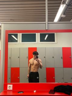 a shirtless man taking a selfie in front of a red and gray locker