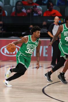 two basketball players in green uniforms running on the court