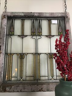 an old stained glass window with red berries hanging from it's sides and a green vase on the other side