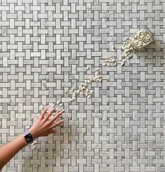 a person reaching for something on the ground with their hand in front of some white tiles