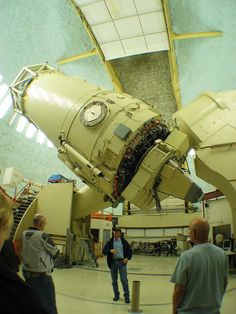 two men standing in front of a large machine with people looking at it and talking