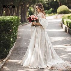 a woman in a wedding dress is standing on the street holding flowers and looking off into the distance