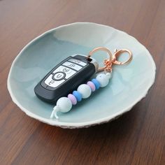 a cell phone keychain sitting on top of a white plate next to a pair of pink and blue beads