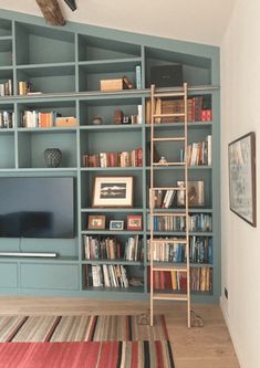 a living room with bookshelves, television and rugs on the hardwood floor