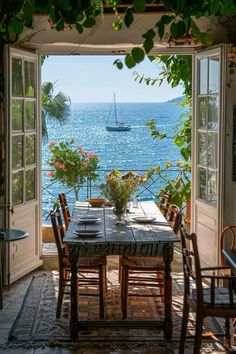 an open door leading to a table with flowers on it and a sailboat in the distance