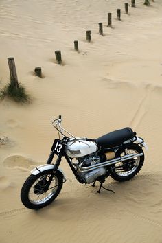 a motorcycle is parked in the sand by some poles and trees on top of it