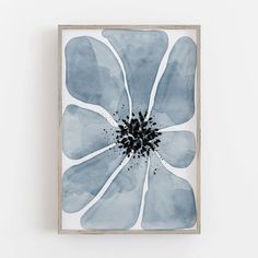 a blue flower with black center in a wooden frame on a white wall above it