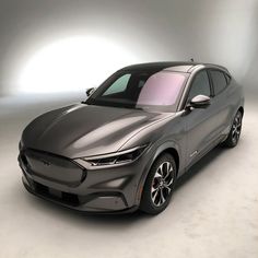 the front end of a grey car in a studio area with light coming from behind it