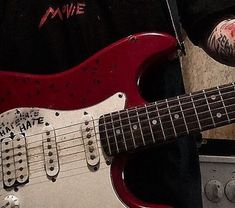 a red electric guitar sitting on top of a hard wood floor next to an amp